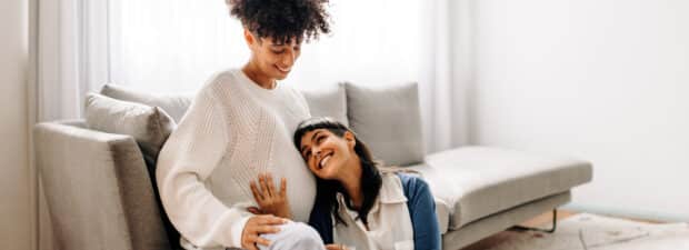 Smiling couple, with one person hugging the other's pregnant belly