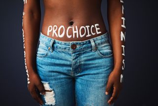 Cropped studio shot of a woman with “pro choice” painted on her stomach against a dark background