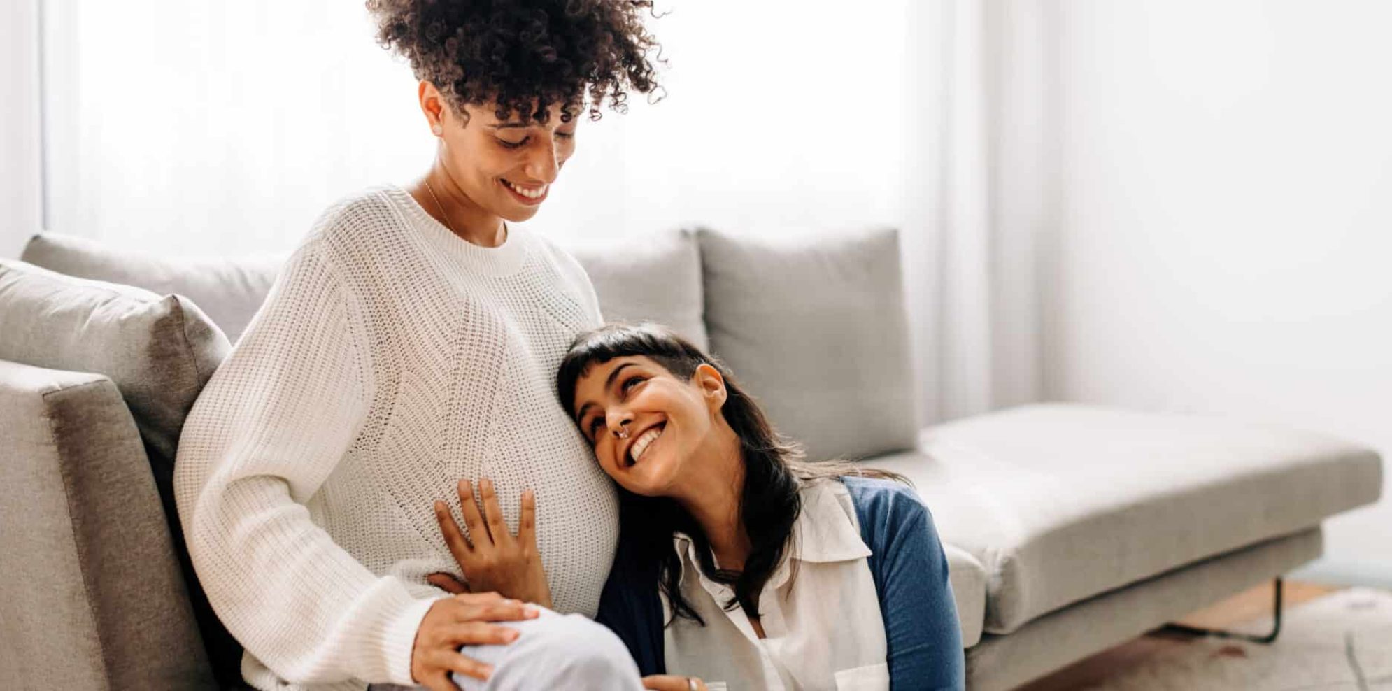 Smiling couple, with one person hugging the other's pregnant belly