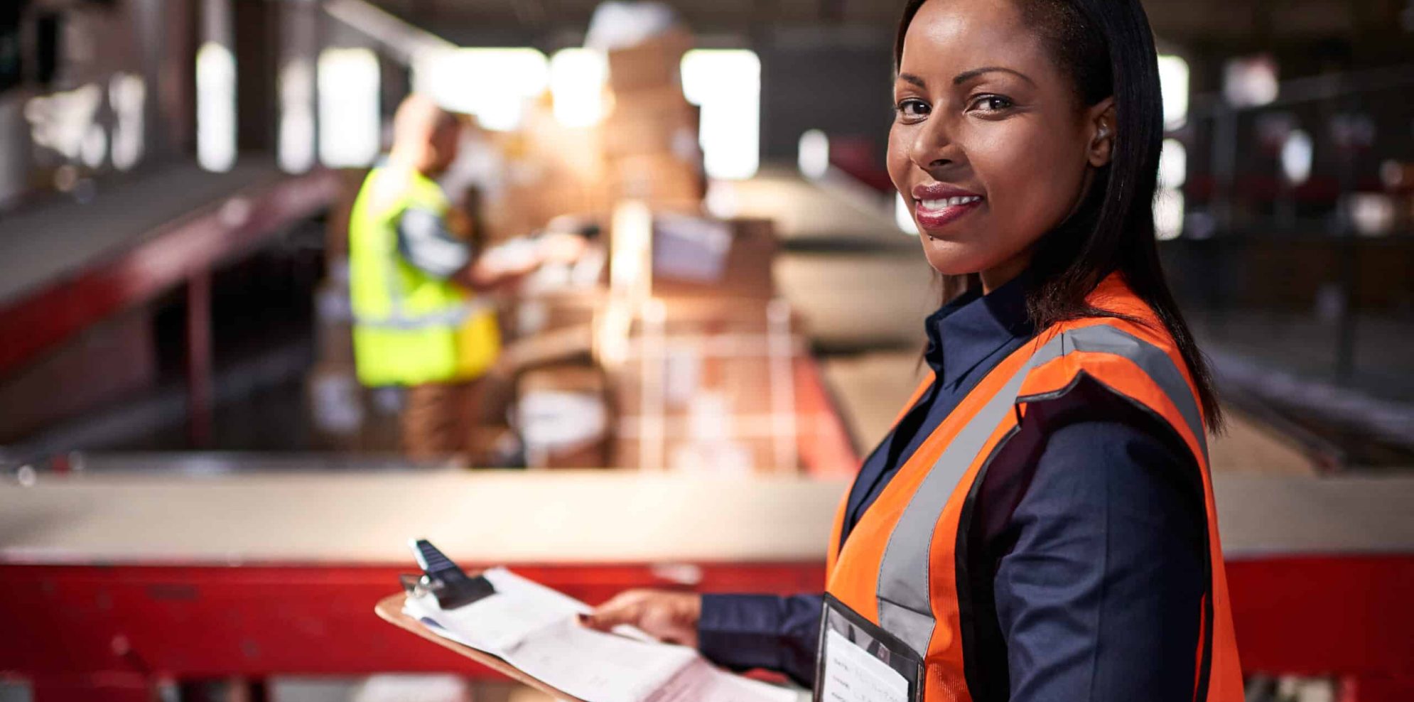 Portrait of a warehouse manager holding a clipboard with workers in the background