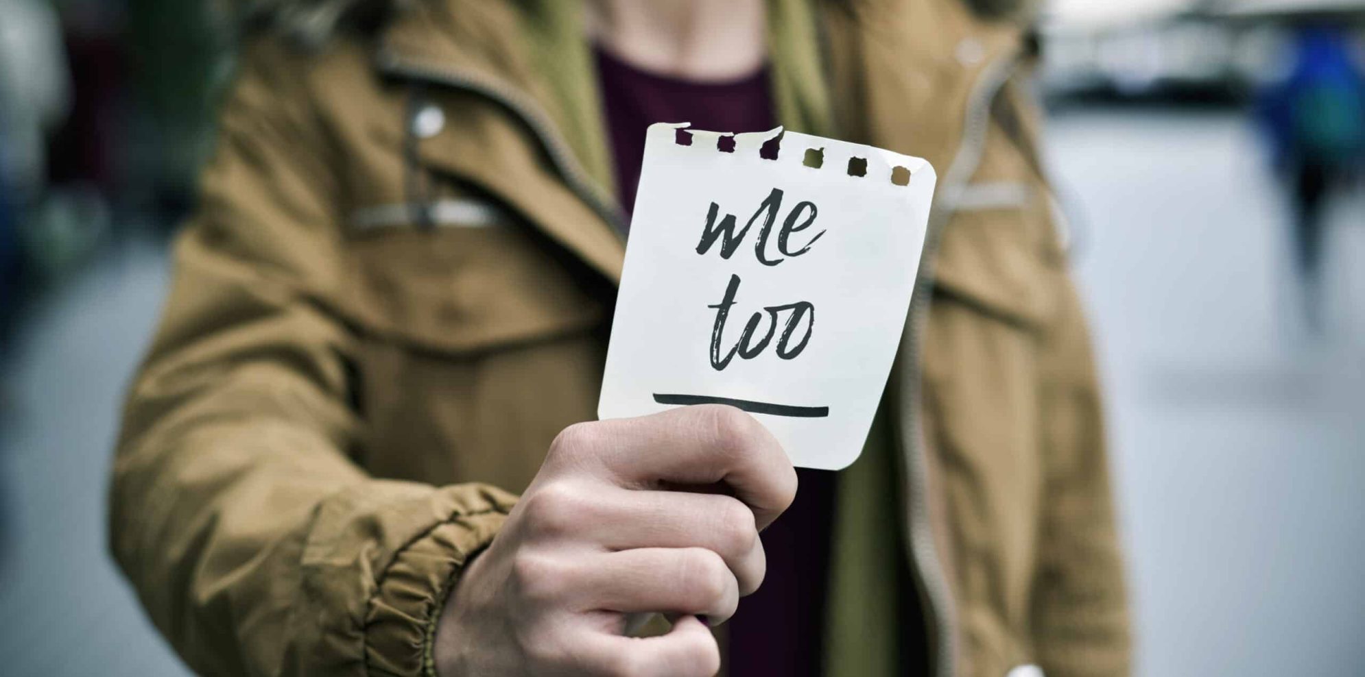 closeup of a young caucasian woman in the street showing a piece of paper with the text me too written in it