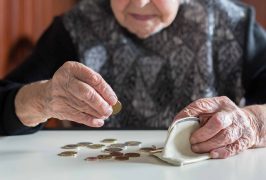 Elderly 95 years old woman sitting miserably at the table at home and counting remaining coins from the pension in her wallet after paying the bills.