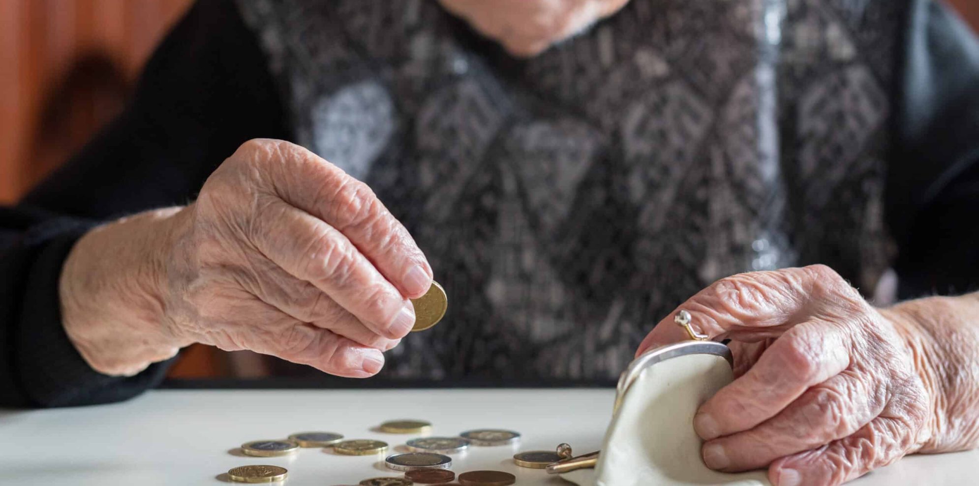 Elderly 95 years old woman sitting miserably at the table at home and counting remaining coins from the pension in her wallet after paying the bills.